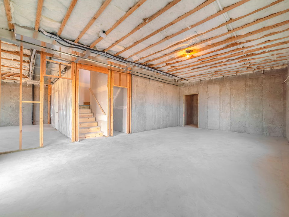 An unlined room in a new house with timber wall framing, insulation between the ceiling joists and conduit runs to a light fitting