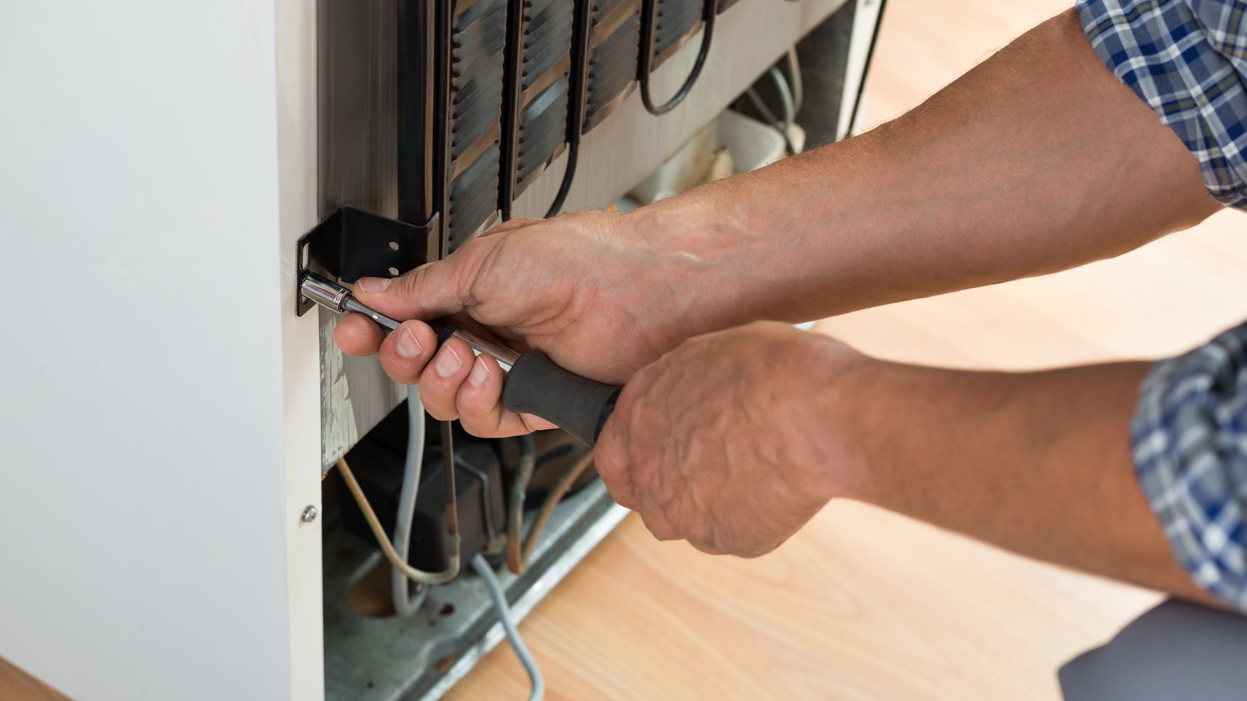 Hands using a screwdriver on the wiring inside an open wall panel