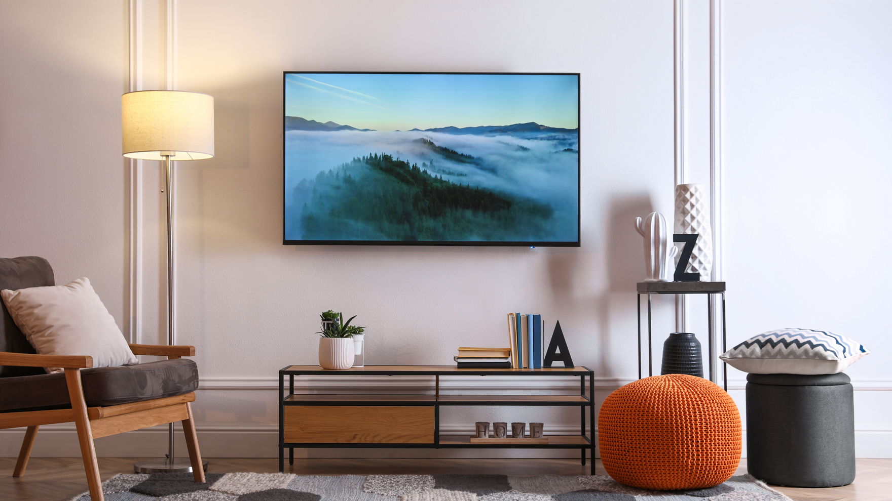 A lounge with a flat-screen television mounted on the wall above a low media cabinet, an armchair and a floor lamp beside it